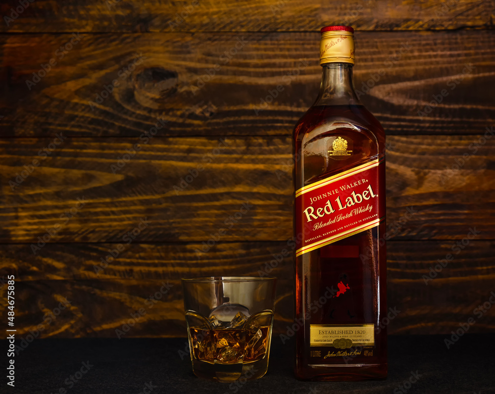 Bottle of Johnnie Walker Red Label Scotch and glass with ice on dark wooden background. Red Label is the most famous Scotch whisky in the world. Stock Photo | Adobe Stock