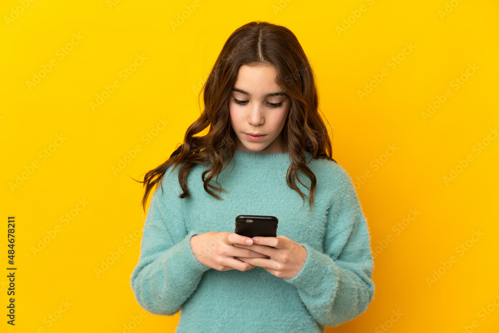 Little caucasian girl isolated on yellow background using mobile phone Little caucasian girl isolated on yellow background using mobile phone