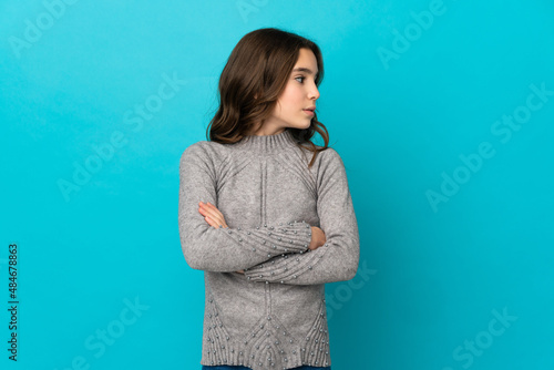Little caucasian girl isolated on blue background keeping the arms crossed