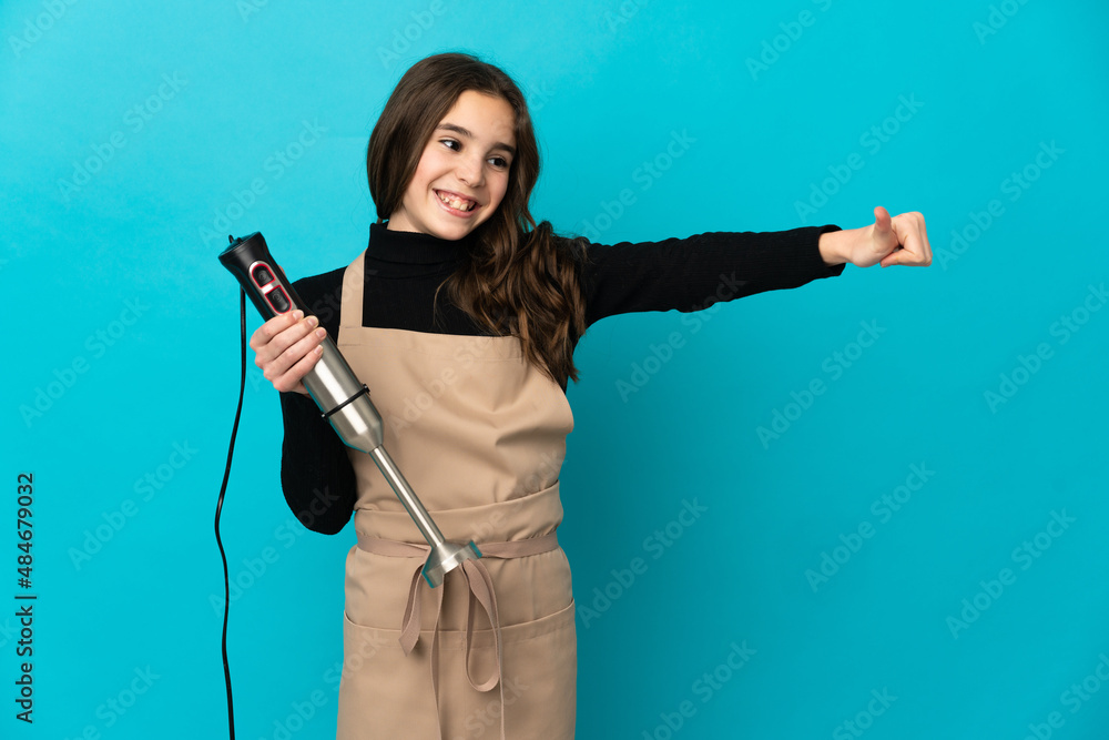 Little girl using hand blender isolated on blue background giving a thumbs up gesture Little girl using hand blender isolated on blue background giving a thumbs up gesture
