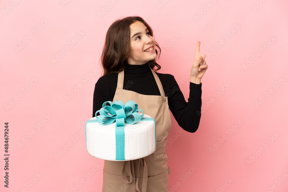 Little Pastry chef holding a big cake isolated on pink background pointing up a great idea Little Pastry chef holding a big cake isolated on pink background pointing up a great idea