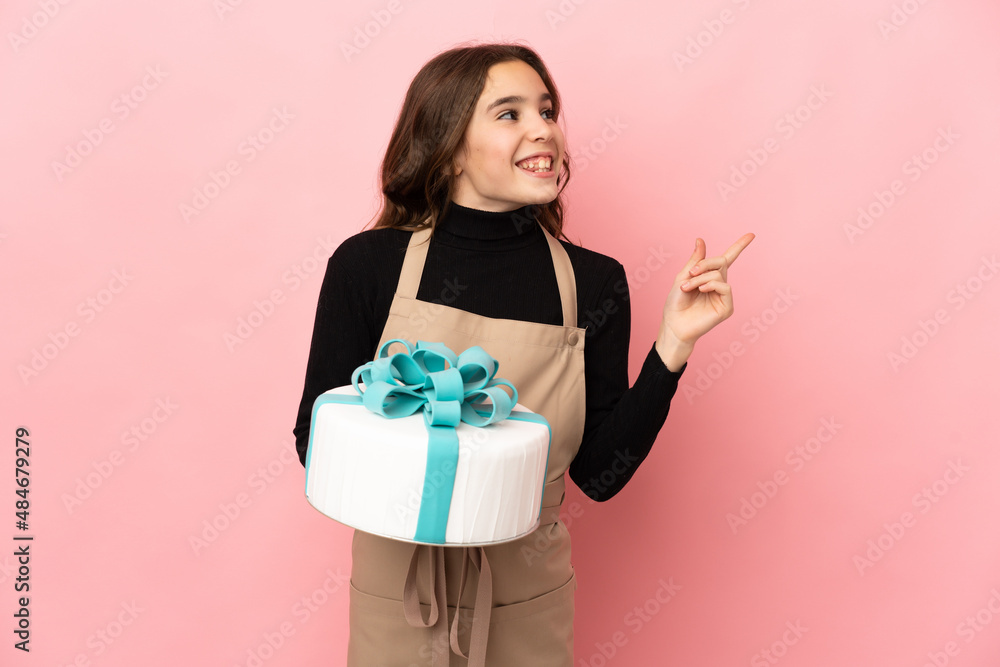 Little Pastry chef holding a big cake isolated on pink background intending to realizes the solution while lifting a finger up Little Pastry chef holding a big cake isolated on pink background intending to realizes the solution while lifting a finger up