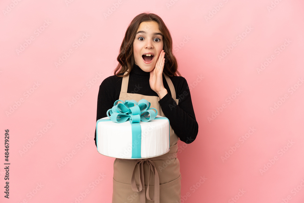 Little Pastry chef holding a big cake isolated on pink background with surprise and shocked facial expression Little Pastry chef holding a big cake isolated on pink background with surprise and shocked facial expression