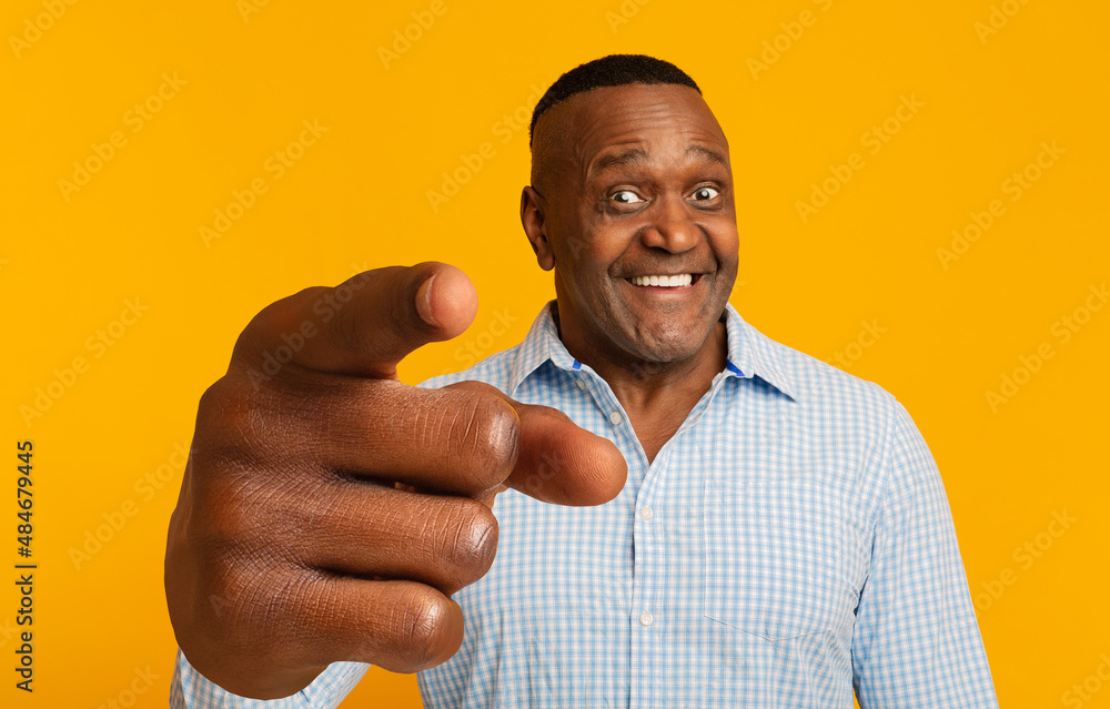 Cheerful mature African American man pointing index finger at camera on orange studio background Cheerful mature African American man pointing index finger at camera on orange studio background