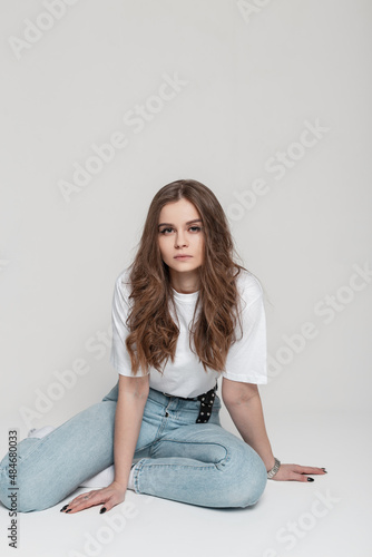 Beautiful young woman with white t-shirt and blue vintage jeans sits in studio on a white background