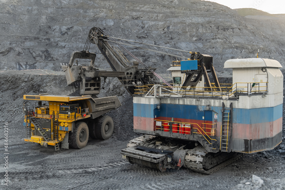 A heavy electric excavator loads ore into a dump truck. The action takes place at night at a gold mining site. A heavy electric excavator loads ore into a dump truck. The action takes place at night at a gold mining site.