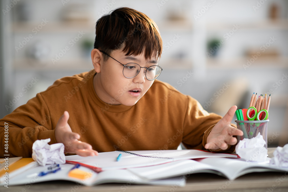 Angry korean teenager looking at exercise book and gesturing Angry korean teenager looking at exercise book and gesturing