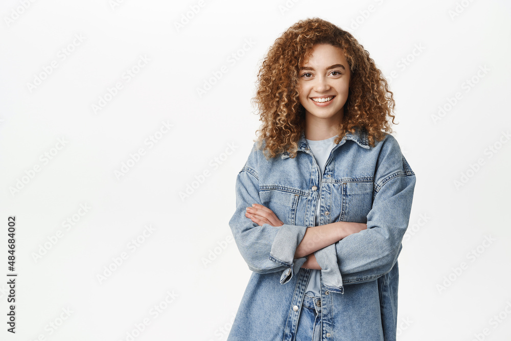Portrait of modern stylish girl with curly hair smiling, standing in casual outfit. Happy young woman posing against white background Portrait of modern stylish girl with curly hair smiling, standing in casual outfit. Happy young woman posing against white background