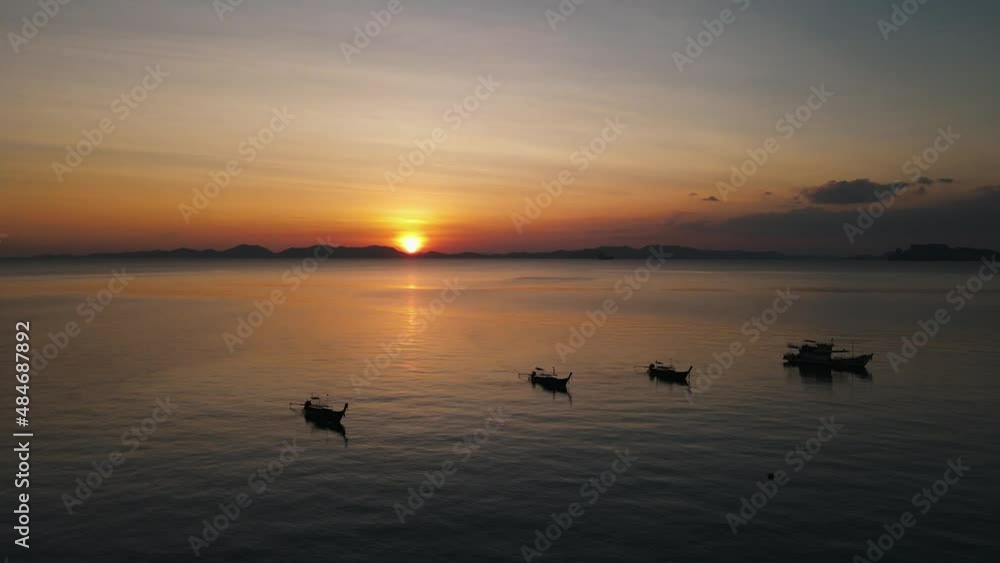 Beautiful sunset over the dark silhouettes of an island, while traditional Thai boats are quietly floating in the foreground. Drone panning shot Beautiful sunset over the dark silhouettes of an island, while traditional Thai boats are quietly floating in the foreground. Drone panning shot