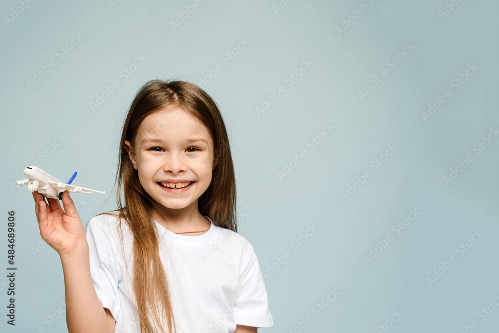 Little girl smiling while holding a fake airplane on a blue background and looking at the camera. Tourism and travel concept. Copy space Little girl smiling while holding a fake airplane on a blue background and looking at the camera. Tourism and travel concept. Copy space
