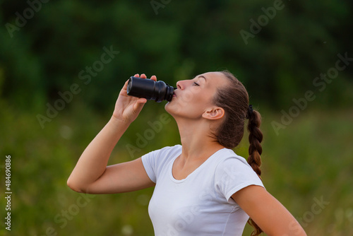 woman drinking water from a plastic bottle on the background of nature