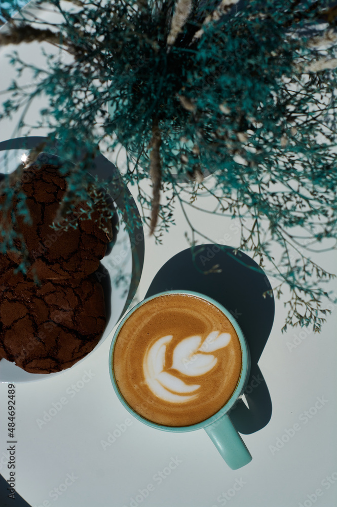 Morning cappuccino in coffee shop on summer terrace with flowers and chocolate cookies.