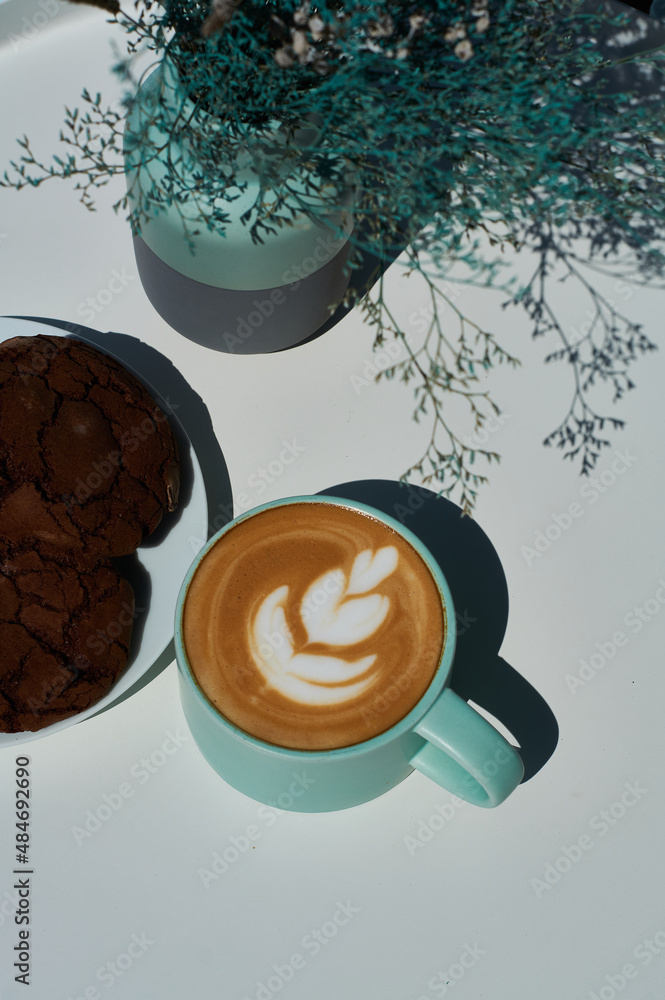 Morning cappuccino in coffee shop on summer terrace with flowers and chocolate cookies.