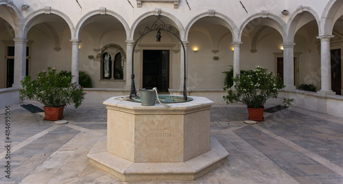 Old fountain on white mediterranean stone in monastery, surrounded with arches photo