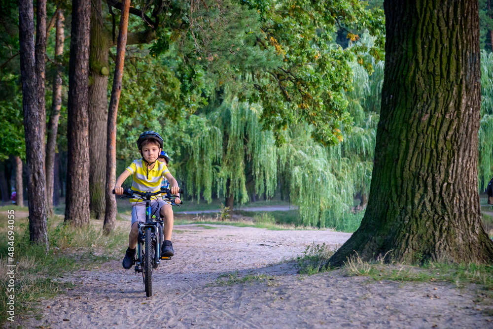 Naklejka premium Portrait of happy toddler child boy riding on bike with helmet. He rides from a small hill, through a sandy forest path. Sport concept: kids ride bicycle first bike active toddler kid
