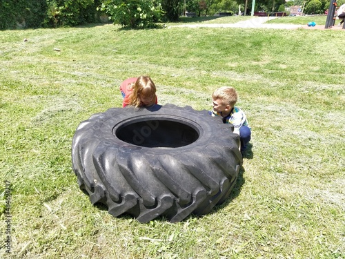 Sremska Mitrovica, Serbia, May 20, 2020. Children play and pick up the tire. Car parts and accessories in a kid's game. A boy and a girl 6 and 7 years old are doing strength exercises on the grass photo