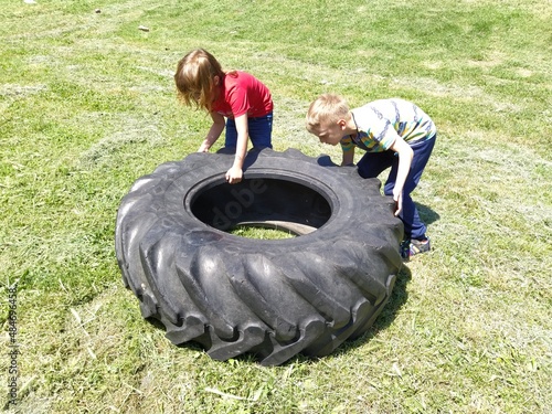 Sremska Mitrovica, Serbia, May 20, 2020. Children play and pick up the tire. Car parts and accessories in a kid's game. A boy and a girl 6 and 7 years old are doing strength exercises on the grass photo