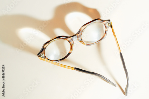 Glasses for old people lie on beige background and cast shadow. View from above. Topic of deterioration of vision with age. Senile myopia. Not fashionable glasses for pensioners.