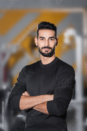 Bearded arabian sportsman looking at camera in blurred sports center.