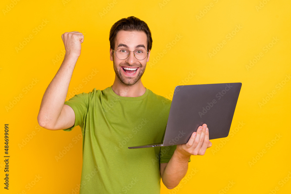 Photo of hooray beard young guy hold laptop hand fist yell wear spectacles green t-shirt isolated on yellow color background Photo of hooray beard young guy hold laptop hand fist yell wear spectacles green t-shirt isolated on yellow color background