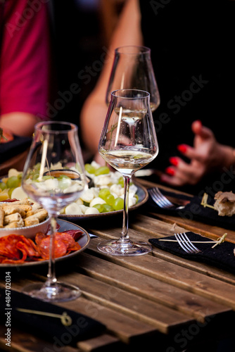 Glasses of wine and plate with fruits and cheese placed on wooden table near chairs on sunny summer day on terrace
