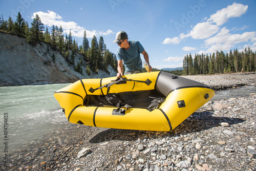 Adventurous man places packraft in river. photo