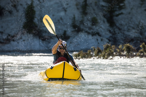 Adventurer paddling packraft on river through canyon. photo