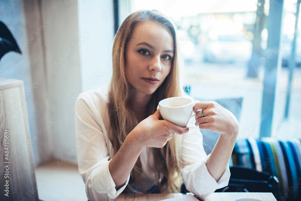 Confident woman with cup of drink near window in cafeteria Confident woman with cup of drink near window in cafeteria