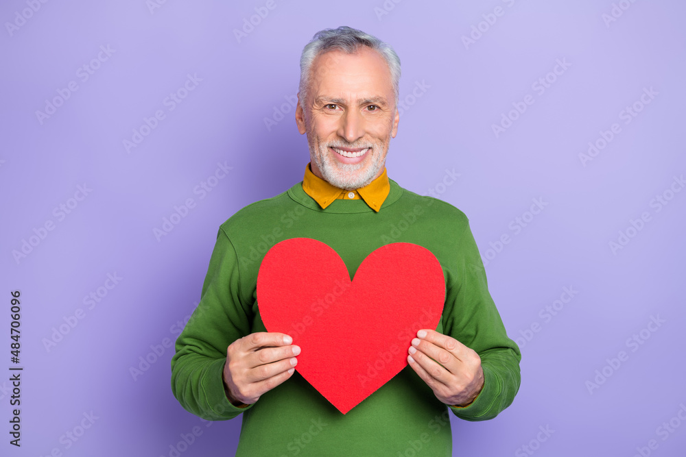 Photo of adorable retired man wear green sweater holding large red heart isolated violet color background Photo of adorable retired man wear green sweater holding large red heart isolated violet color background