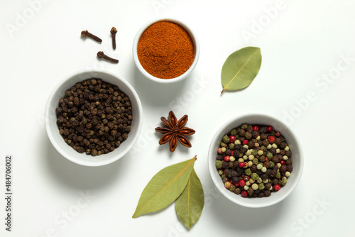Spices assorted colorful peppercorns and powder paprika in bowls and bay leaf, anise, clove on white background.