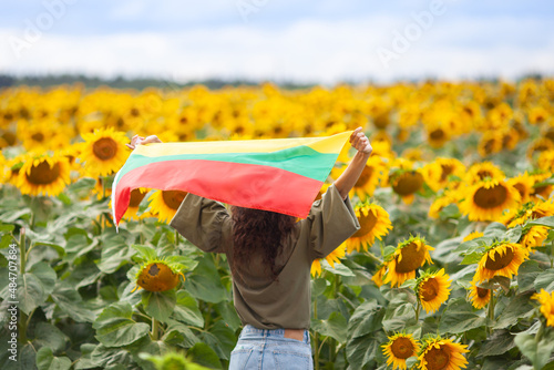 Woman holding flag of Lithuania in a sunflowers field. Back view. Lithuanian Flag Day. Independence restoration Day. Travel and love Lithuania concept. Selective focus. photo