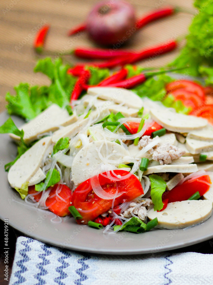 Spicy Glass Noodle Salad with Vietnamese Sausage served in a gray plate Put on a wooden table and various vegetables. Spicy Glass Noodle Salad with Vietnamese Sausage served in a gray plate Put on a wooden table and various vegetables.