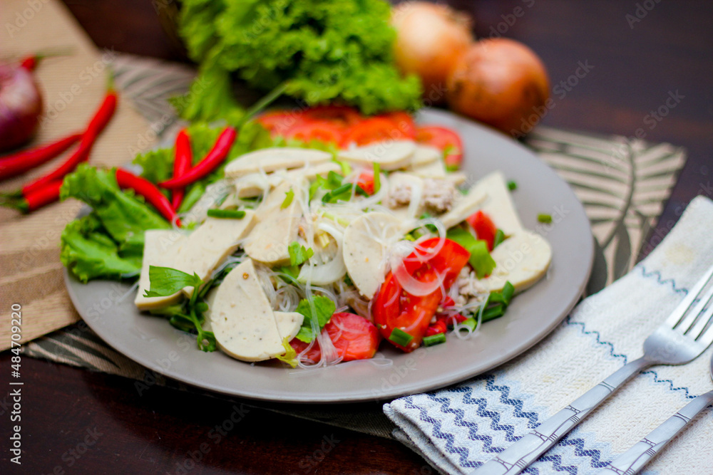 Spicy Glass Noodle Salad with Vietnamese Sausage served in a gray plate Put on a wooden table and various vegetables. Spicy Glass Noodle Salad with Vietnamese Sausage served in a gray plate Put on a wooden table and various vegetables.