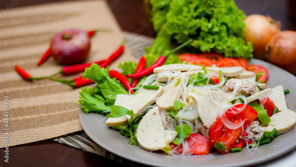 Spicy Glass Noodle Salad with Vietnamese Sausage served in a gray plate Put on a wooden table and various vegetables. Spicy Glass Noodle Salad with Vietnamese Sausage served in a gray plate Put on a wooden table and various vegetables.