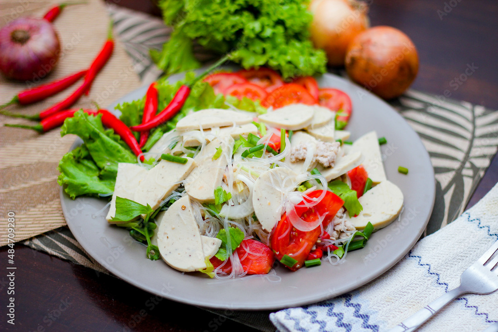 Spicy Glass Noodle Salad with Vietnamese Sausage served in a gray plate Put on a wooden table and various vegetables. Spicy Glass Noodle Salad with Vietnamese Sausage served in a gray plate Put on a wooden table and various vegetables.