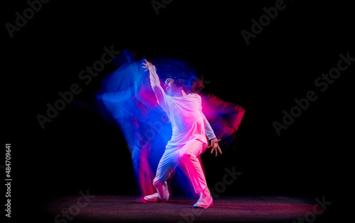 Dynamic portrait of male hip-hop dancer dancing isolated on dark background in mixed neon light. Youth culture, hip-hop, movement, style and fashion, action.