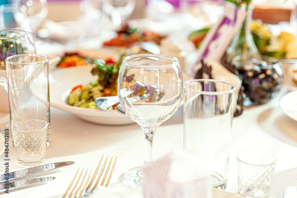 Fancy table set for dinner with napkin glasses in restaurant, luxury interior background. Wedding elegant banquet decoration and items for food arranged by catering service on white tablecloth table Fancy table set for dinner with napkin glasses in restaurant, luxury interior background. Wedding elegant banquet decoration and items for food arranged by catering service on white tablecloth table