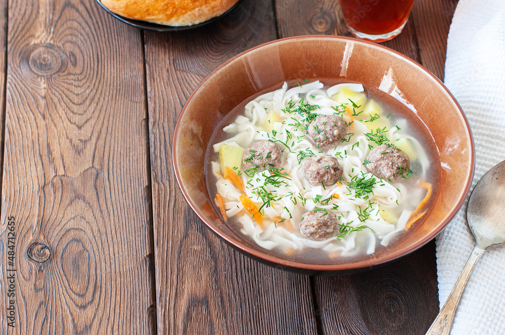 Homemade meatballs soup with noodles in a bowl on a wooden background.
