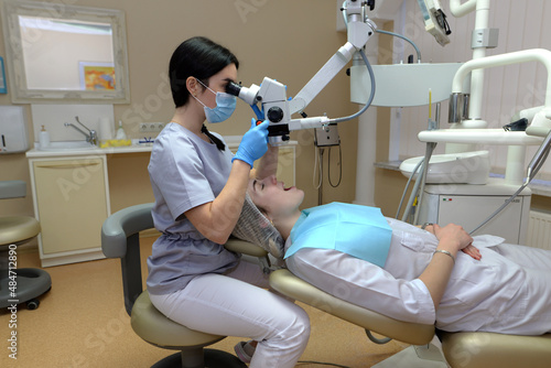 Young woman dentist treating root canals using microscope in the dental clinic. Man patient lying on dentist chair with open mouth. Medicine  dentistry and health care concept.