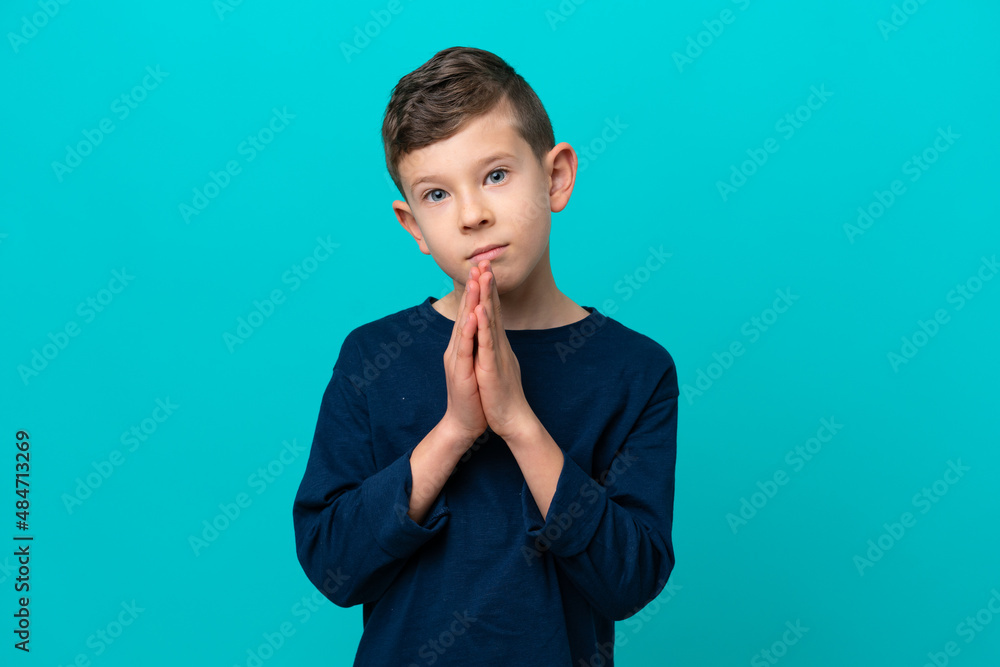Little kid boy isolated on blue background keeps palm together. Person asks for something Little kid boy isolated on blue background keeps palm together. Person asks for something