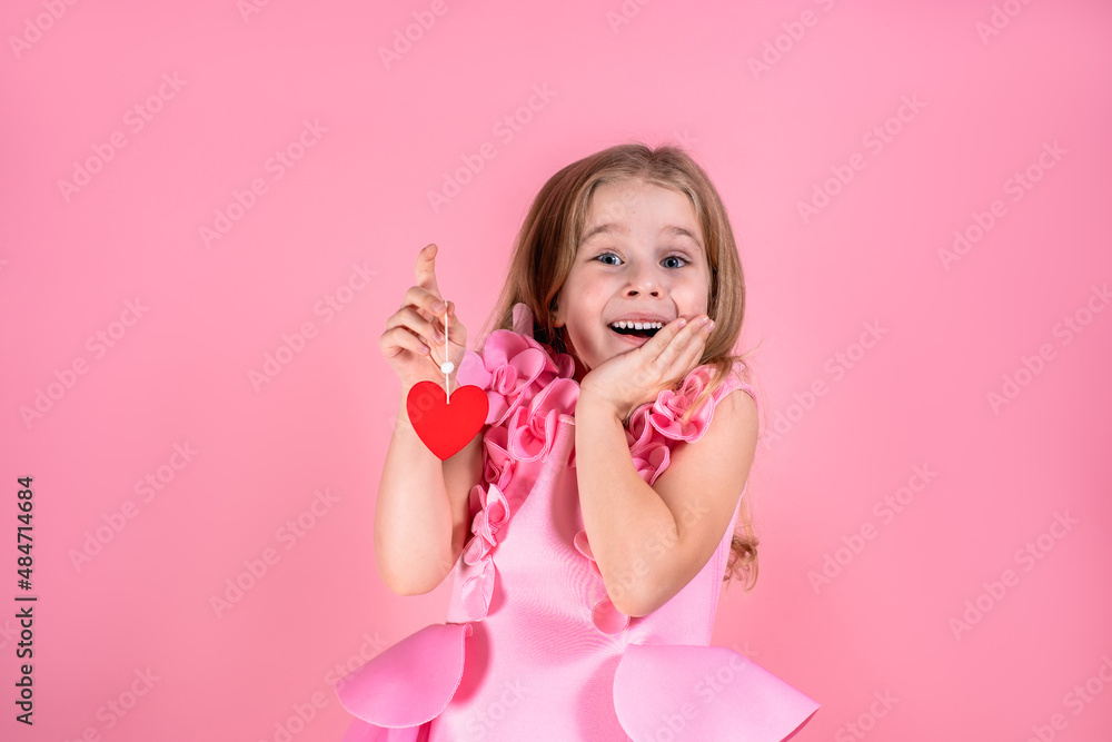 Portrait of astonished beautiful little blue-eyed girl with long fair hair in chic pink dress stand smiling holding red paper heart on string on pink background. Valentines day, love, emotion concept. Portrait of astonished beautiful little blue-eyed girl with long fair hair in chic pink dress stand smiling holding red paper heart on string on pink background. Valentines day, love, emotion concept.