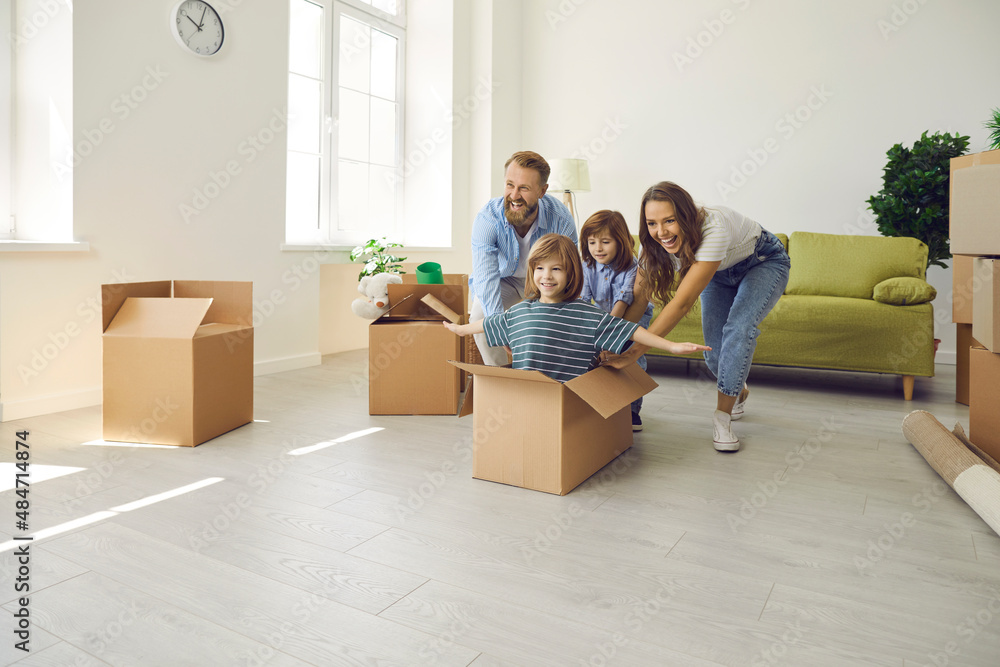 Happy family with children having fun in new home. Excited first-time buyers laughing and playing with boxes in spacious living room interior. Real estate, residential mortgage, buying house concept Happy family with children having fun in new home. Excited first-time buyers laughing and playing with boxes in spacious living room interior. Real estate, residential mortgage, buying house concept