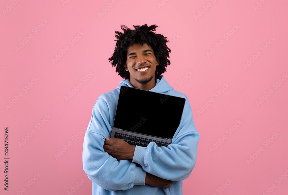 Cool black teenager in casual wear hugging laptop pc with mockup for design on empty screen over pink background Cool black teenager in casual wear hugging laptop pc with mockup for design on empty screen over pink background