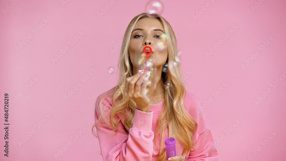 Fototapeta premium Blonde woman blowing soap bubbles isolated on pink.