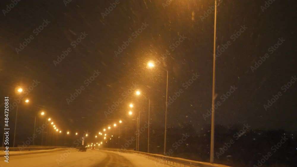 Snow falling at night on an empty road, no traffic, a row of bright street lights Snow falling at night on an empty road, no traffic, a row of bright street lights