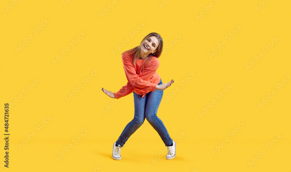 Funny carefree beautiful young woman having fun. Happy pretty teenage girl in comfortable casual wear looking at camera and smiling while dancing in the studio against vibrant yellow colour background Funny carefree beautiful young woman having fun. Happy pretty teenage girl in comfortable casual wear looking at camera and smiling while dancing in the studio against vibrant yellow colour background