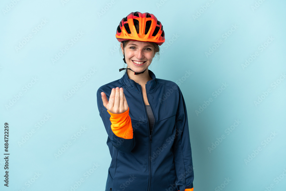 Young cyclist woman isolated on blue background inviting to come with hand. Happy that you came - obrazy, fototapety, plakaty 