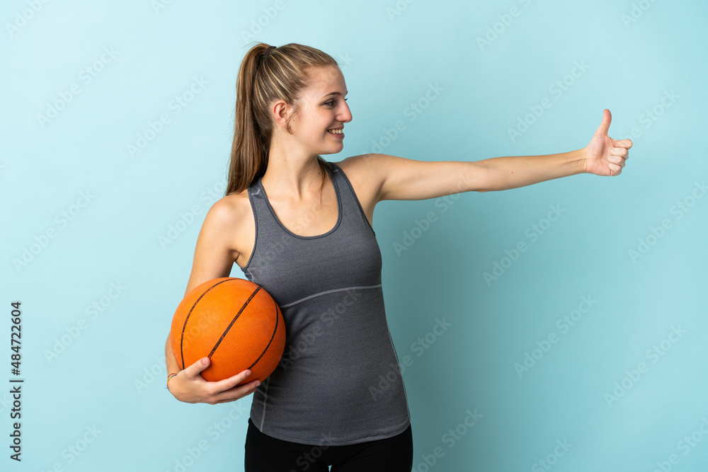 Young woman playing basketball isolated on blue background giving a thumbs up gesture Young woman playing basketball isolated on blue background giving a thumbs up gesture