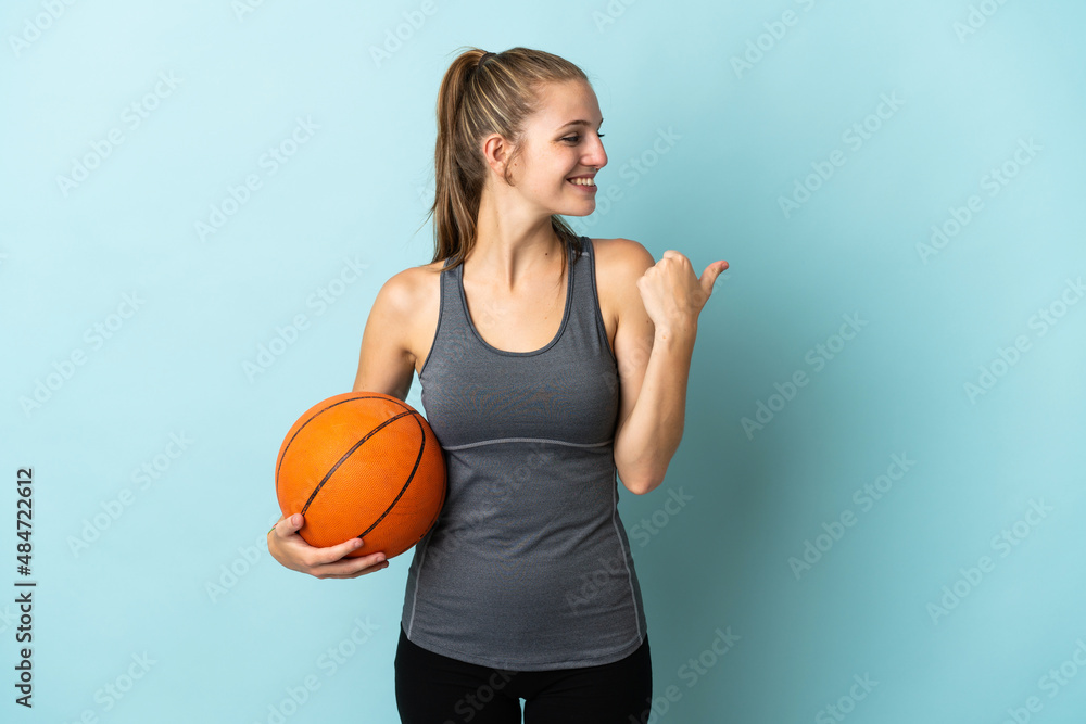 Young woman playing basketball isolated on blue background pointing to the side to present a product