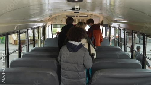 Back view of multinational secondary school pupils wearing medical masks standing in aisle and taking turns getting off school bus. Diverse students in face masks leaving school bus one after another photo